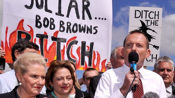 Abbott ante dos carteles que tildan a la primera ministra de bitch (zorra) y witch (bruja). / THE AUSTRALIAN