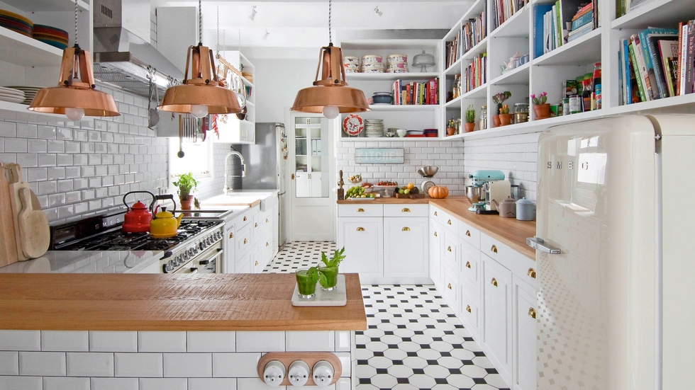 Dos ideas organizan la cocina: sustituir los armarios superiores por estanterías y utilizar el mosaico de azulejos (de Via Ceramica) para ir abriendo el espacio hacia el salón. La madera de las encimeras y las lámparas de bronce, adquiridas en un anticuario francés, añaden calidez. Los fogones y la nevera son de Smeg.