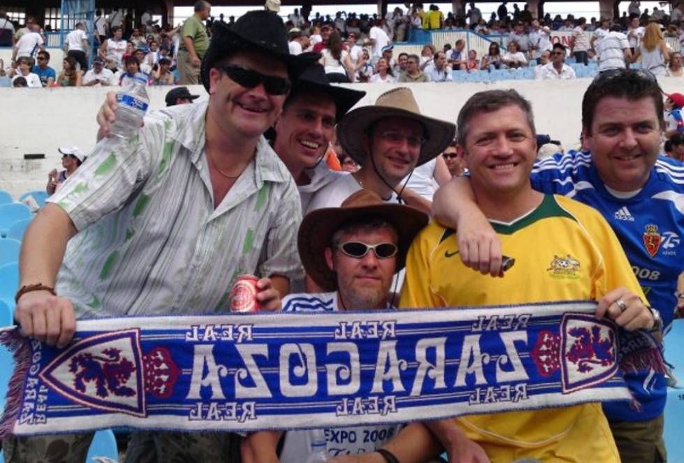 Jason Morris lleva 24 años alargando su estancia temporal en Zaragoza. Dos más de los que cuenta como seguidor del Real Zaragoza. Morris llegó a la capital aragonesa para impartir clases de educación física en un campamento de verano en 1994. Tras acabar la carrera, en 1996, decidió que se quedaría un añito. "Y así uno tras otro hasta hoy, que ya no pienso marcharme", comenta. Se aficionó al fútbol local enseguida y, en 2000, este británico nacido en Alemania, se hizo socio del Real Zaragoza. Su corazón, sin embargo, está partido en tres querencias. "He sido gran forofo del equipo alemán Borussia Mönchengladbach, pero también del Liverpool", agrega. Morris recuerda la final del año 1977 en el que ambos equipos se vieron las caras. "Ganó el Liverpool", añade y asegura que muchos británicos saben que existe Zaragoza porque en 1995 ganó al Arsenal 2-1, aunque pocos saben ubicarla en el mapa. “Yo tampoco antes de venir aquí”, concluye.  En la foto: Jason (izquierda) con sus amigos durante un partido.