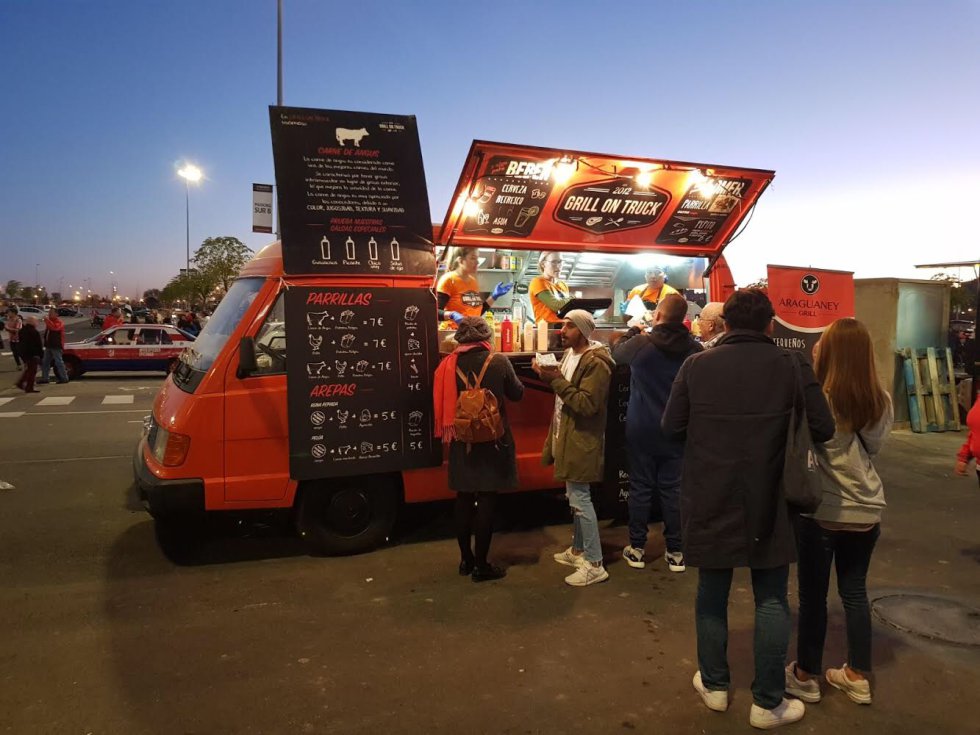 La mudanza del Atlético de Madrid del Vicente Calderón al Wanda Metropolitano en 2017 acabó con el ceremonial previo a los partidos. Las tapas en La Latina eran una parada obligada. Ahora, la nueva casa de los rojiblancos alberga otras costumbres. Decenas de food trucks se agolpan alrededor del moderno estadio. Llegar con antelación a la cita se ha convertido en un ritual para los hinchas colchoneros. Grill On Truck, el camión de comida de la venezolana Marbell Pérez (a la izquierda en la imagen), es una de las paradas favoritas de algunos aficionados atléticos. ¿La carta? Parrillitas, pepitos, tequeños y arepas. “El primer día en el Wanda designaron el puesto en la zona infantil, cuando en realidad se suponía que estaríamos en la zona ‘caliente’. No esperábamos que viniera tanta gente. Nos vimos sobrepasados. ¡Había una fila de más de 50 personas!”, recuerda sobre su primera vez en las inmediaciones del coliseo rojiblanco.