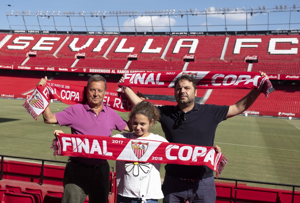 El día que hay partido, Cayetana García llega pronto a casa de su padre, David García, en el barrio sevillano de La Macarena. La muchacha, de 12 años, les azuza a él y a su abuelo Rafael para no demorarse en salir hacia el estadio. “Lo hace porque sabe que yo siempre voy muy justo de tiempo, es muy pesada”, confiesa David. Ya en el Ramón Sánchez-Pizjuán ocupan sus asientos en Preferencia, los tres juntos porque se han hecho con un pack familiar que promociona el Sevilla. “Con esta oferta nos cuesta lo mismo que si solo fuéramos abonados mi padre y yo”, afirma.   Cuando el Sevilla juega fuera, la familia ve el partido en el Colmao, el bar que regenta David. Él siente los colores casi desde que nació. “Mi padre nos llevaba a mí y mis tres hermanos de pequeños al campo”. La pasión de su hija por el club, sin embargo, le pilló por sorpresa. “Nunca le metí el fútbol en vena”, bromea David. Ella mantiene en forma el espíritu sevillista familiar. “El exceso de trabajo y el cansancio me estaban quitando las ganas de seguir yendo al campo”, confiesa el padre. “Es ella la que me motiva”, agrega sobre Cayetana, que nunca pierde el aliento, incluso ante las derrotas más duras. “El día de la final con el Barça, metiéndonos cinco goles a cero, mi padre y yo, callados, contemplábamos a mi hija cantando como loca las canciones y diciéndonos que el resultado daba igual”.    En la foto: Rafael, David y Cayetana García.