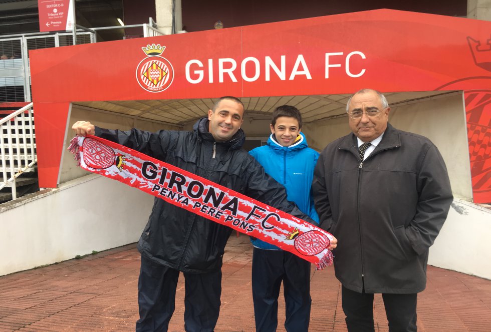Jan Nadal, de 13 años, observa cada partido del Girona FC como un experto analista. Se permite criticar tanto la actuación del árbitro como la de los jugadores. “Incluso aporta sus propias acotaciones técnicas”, comenta su abuelo, Joaquim Nadal, de 70 años, que fue alcalde socialista de la ciudad entre 1979 y 2002. Jan va habitualmente al estadio Municipal de Montilivi con su abuelo, su hermano Nil y sus padres. Juntos han compartido grandes momentos en el recinto, como el ascenso del club de sus amores a LaLiga Santander hace dos temporadas. Ahora, antes de emitir su opinión, Jan espera a lo que tenga que decir el VAR.   “Vivimos el ascenso como un movimiento ciudadano”, relata Raimon Nadal, empleado del sector maderero de 42 años, padre de Jan. Lo que antes había sido un club de afición local y minoritaria se convertía en un fenómeno de masas. “Empezamos a ver a gente con la camiseta del Girona por la calle”, recuerda. Sus hijos sienten los colores desde mucho antes: son socios desde que nacieron, periodo que coincide con el ascenso a LaLiga 1|2|3. Ahora también son abonados. Poco se parece este Girona al que Joaquim conoció de pequeño. “Un amigo de la familia nos dejaba un carné para entrar, era en la parte de arriba del antiguo estadio Vistalegre”, rememora. Entonces, con el Girona en Tercera, se vivía de manera diferente. “He visto a un cura, profesor de mi instituto, saltar al campo con la sotana levantada para pegar al árbitro”, añade.    En la foto: Raimon, Jan y Joaquim Nadal en el campo del Girona Fútbol Club.
