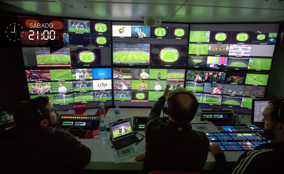 Óscar Lago es uno de los más reputados realizadores del planeta fútbol. “El mejor”, aseguran una y otra vez sus cámaras. Ha dado indicaciones a todos, pero controla en directo qué está grabando cada uno: las pantallas en las que ve la señal de las 27 cámaras llevan el nombre de quien las opera: Chucky, Pepe, Alfredo, Inés… Lago, sin descanso, va indicando: “Pasamos a la seis; árbitro, Oliva”. Cuando faltan 30 segundos para el saque inicial pincha la señal del helicóptero de nuevo: “Diego, despacio, zoom out”. Luego, cámara aérea. Se produce el saque. Empieza el partido.