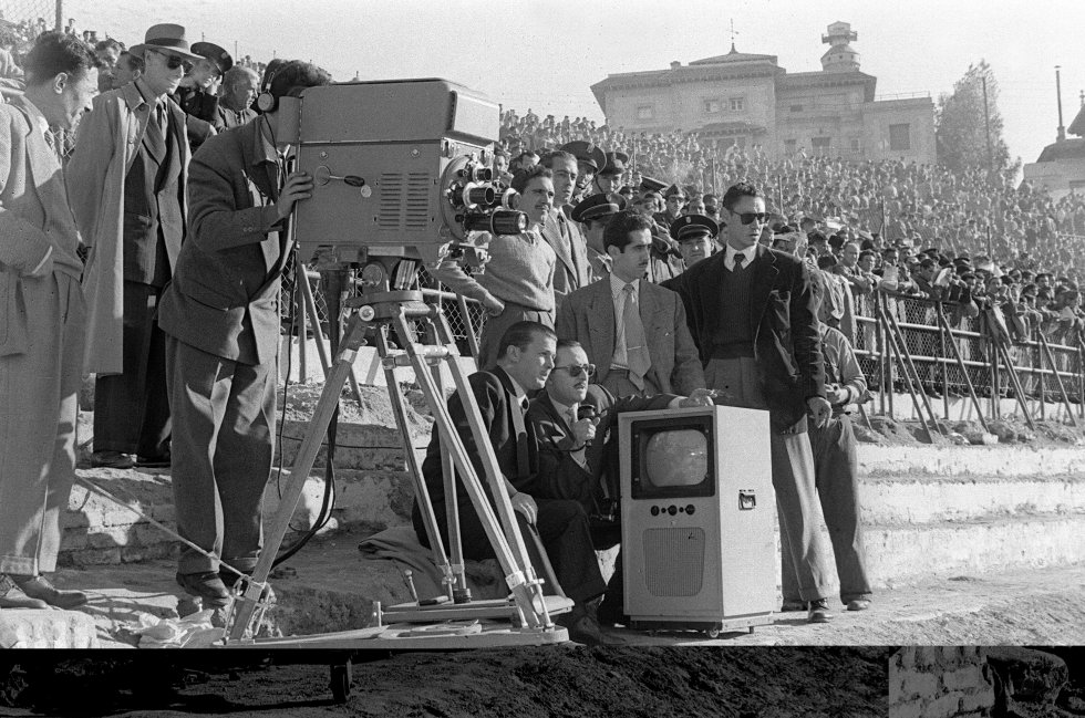El primer partido televisado en España fue un Real Madrid - Racing de 1954, con TVE aún en emisiones de prueba. “Solo se vio en Madrid. El primero que llegó a Barcelona fue el Real Madrid - FC Barcelona de 1959, semanas después de que se inaugurase el repetidor de La Muela (Zaragoza), que permitía enviar contenido entre las dos ciudades”, rememora Alfredo Relaño. Los televisores se agotaron en la capital catalana. Una agencia acordó con los bares pagarles la mitad del aparato si dejaban un cartel con un anuncio sobre el televisor. Hubo cafeterías que incluso cobraron entrada. Ya entonces había varias cámaras colocadas en diferentes posiciones del estadio para captar toda la acción del juego, eso sí, en blanco y negro. Más tarde se llegaría a instituciomalizar la retransmisión por la televisión única, TVE, de un partido cada jornada por la noche, cuando ya hubiera acabado el resto. En la imagen, las cámaras de Televisión Española retransmiten el encuentro de la temporada 195455 entre el Atlético de Madrid y el Sevilla en el Metropolitano.