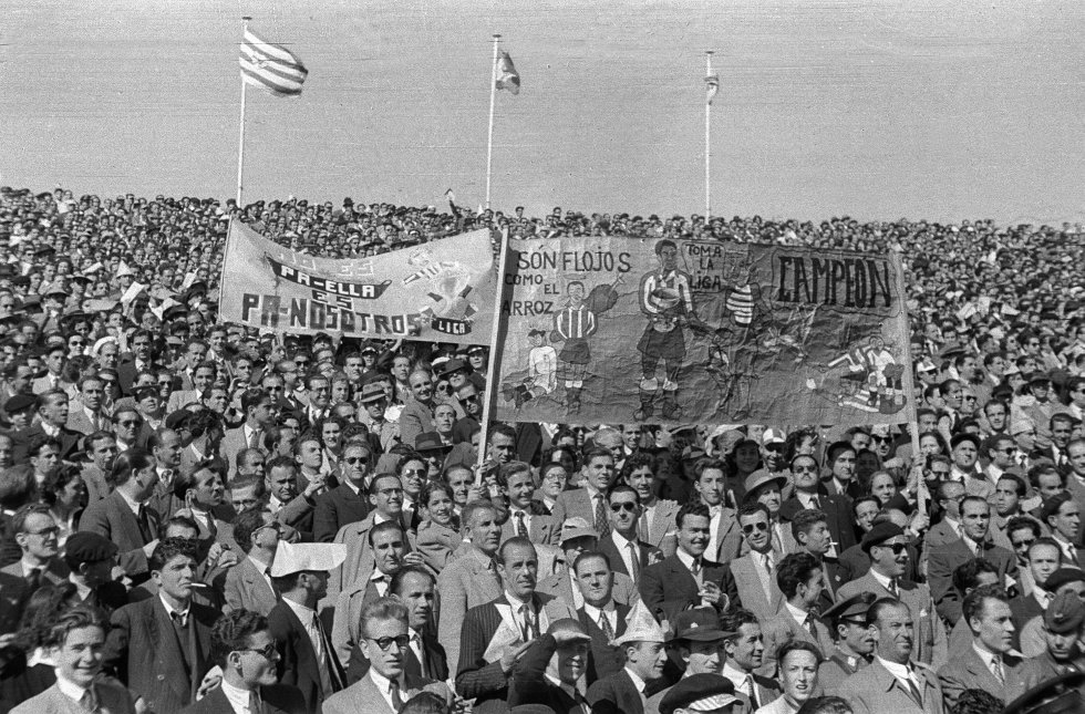 23 de abril de 1950. El público de un Metropolitano abarrotado anima con pancartas al Atlético de Madrid en el encuentro liguero ante el Valencia, tras el cual el conjunto rojiblanco se proclama campeón. Todos están de pie. Visten sus mejores galas. Algunos, incluso, de uniforme. “Los partidos solían jugarse los domingos y eran un acontecimiento social. Era como ir a misa, no se podía ir de cualquier manera”, cuenta el director del diario As, Alfredo Relaño. Prácticamente todos los espectadores del fútbol eran hombres. Algunos llevan un cartucho de papel en la cabeza, muy habituales los días de sol. Los vendedores ambulantes ofrecían tabaco y copas de coñac. Las pancartas, más artesanales que las actuales, apuntan al rival con tono despectivo, seguramente sancionable hoy. “Los cánticos eran variaciones repetidas del nombre del equipo, como ‘¡Racing! ¡Racing! ¡Ra! ¡Ra! ¡Ra!”, destaca Relaño. El paisaje en la grada comenzó a cambiar cuando los jóvenes empezaron a ocupar los fondos de los estadios, hacia mediados de los años 70.