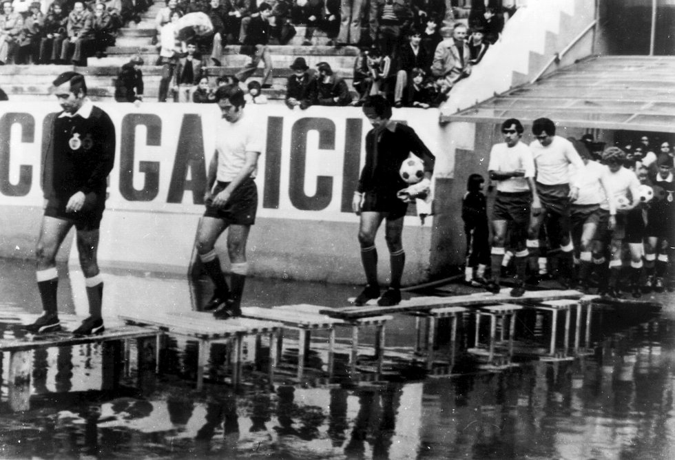 Patatal. Barrizal. Terreno impracticable. Estas expresiones eran comunes en nuestro fútbol hasta hace muy pocos años. Ciertos estadios tenían fama de transformarse con las inclemencias del tiempo y originaban estampas que parecían más propias de un campo de batalla. Aquello provocaba lesiones e influía decisivamente en el tipo de juego que se practicaba. Había muy poca normativa: si los dos equipos querían jugar y el colegiado lo aprobaba, podía jugarse un partido sobre la nieve. El barro era un aliado en la estrategia de los equipos de las zonas más lluviosas. En la imagen, la entrada al campo de jugadores y cuerpo arbitral en un Celta-UD Las Palmas de la temporada 197677.