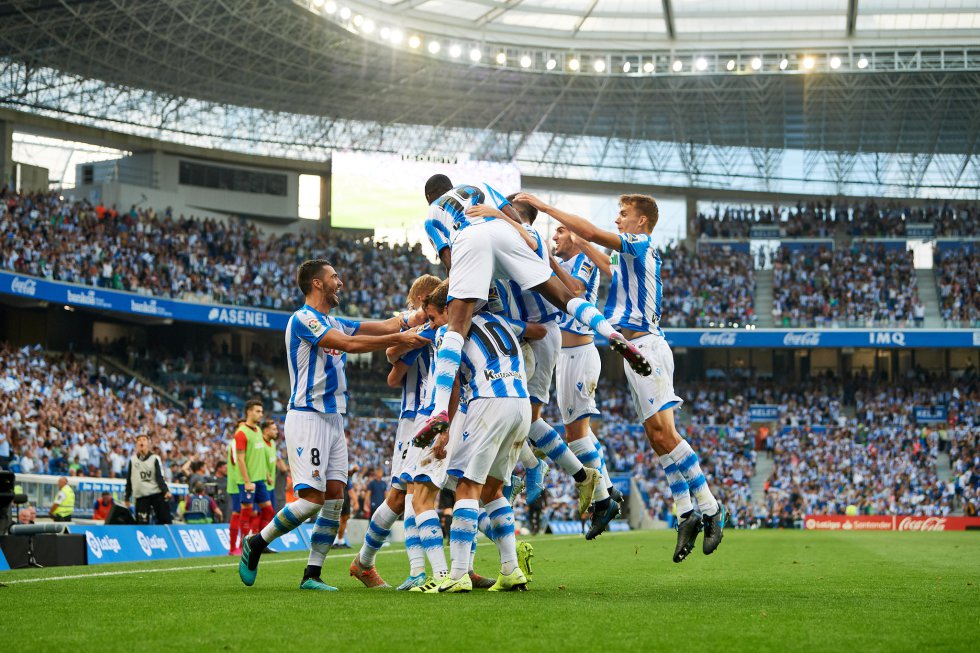 Ocho metros separan ahora la grada del césped del Reale Arena (Anoeta). La remodelada casa de la Real Sociedad, que ahora alberga a 40.000 'txuri-urdines' (8.000 más que antes) ha sido la gran novedad del equipo esta temporada. Atrás quedó la fría pista de atletismo y a San Sebastián regresó aquella cercanía de las épocas gloriosas del viejo campo de Atotxa. Otro estadio de primera categoría se suma al remodelado Benito Villamarín (2017), o a los nuevos Wanda Metropolitano (2017), San Mamés (2013) o RCDE Stadium (2009). Después del Reale Arena, la competición seguirá creciendo con proyectos que ya están en marcha: el Santiago Bernabéu, el Camp Nou, Abanca-Balaídos o Abanca-Riazor forman parte de esa lista. En la imagen, el equipo celebra uno de los goles en la victoria por 3 a 0 frente al Atlético de Madrid.